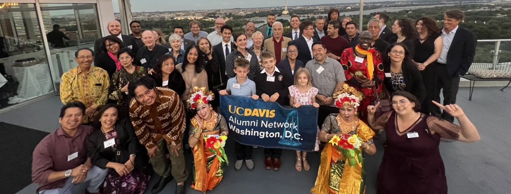 A group of UC Davis community members pose on the rooftop in front of the Potomac River in the horizon.