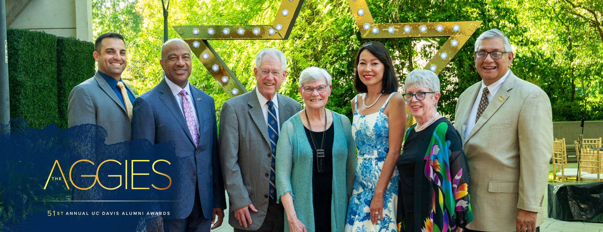 Chancellor Gary May and CAAA Board President Scott Judson pose with Alumni Award winners Bob and Cathy Kerr, Adriana Gascoigne, Sandy Reed, and Neptaly "Taty" Aguilera in front of a large gold marquee archway..