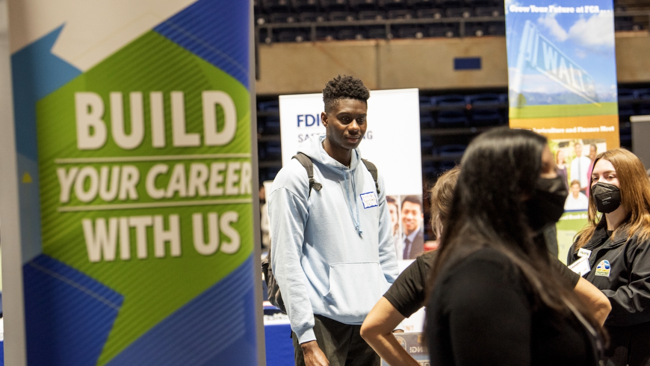 A man is standing in the career fair. In front of him is a sign saying "Build Your Career With Us'.