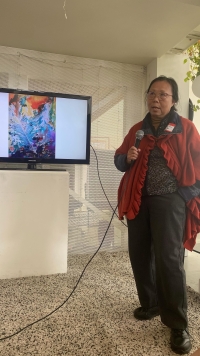 Qinqin Liu, UC Davis alumni artist stands holding microphone next to a mounted TV screen.