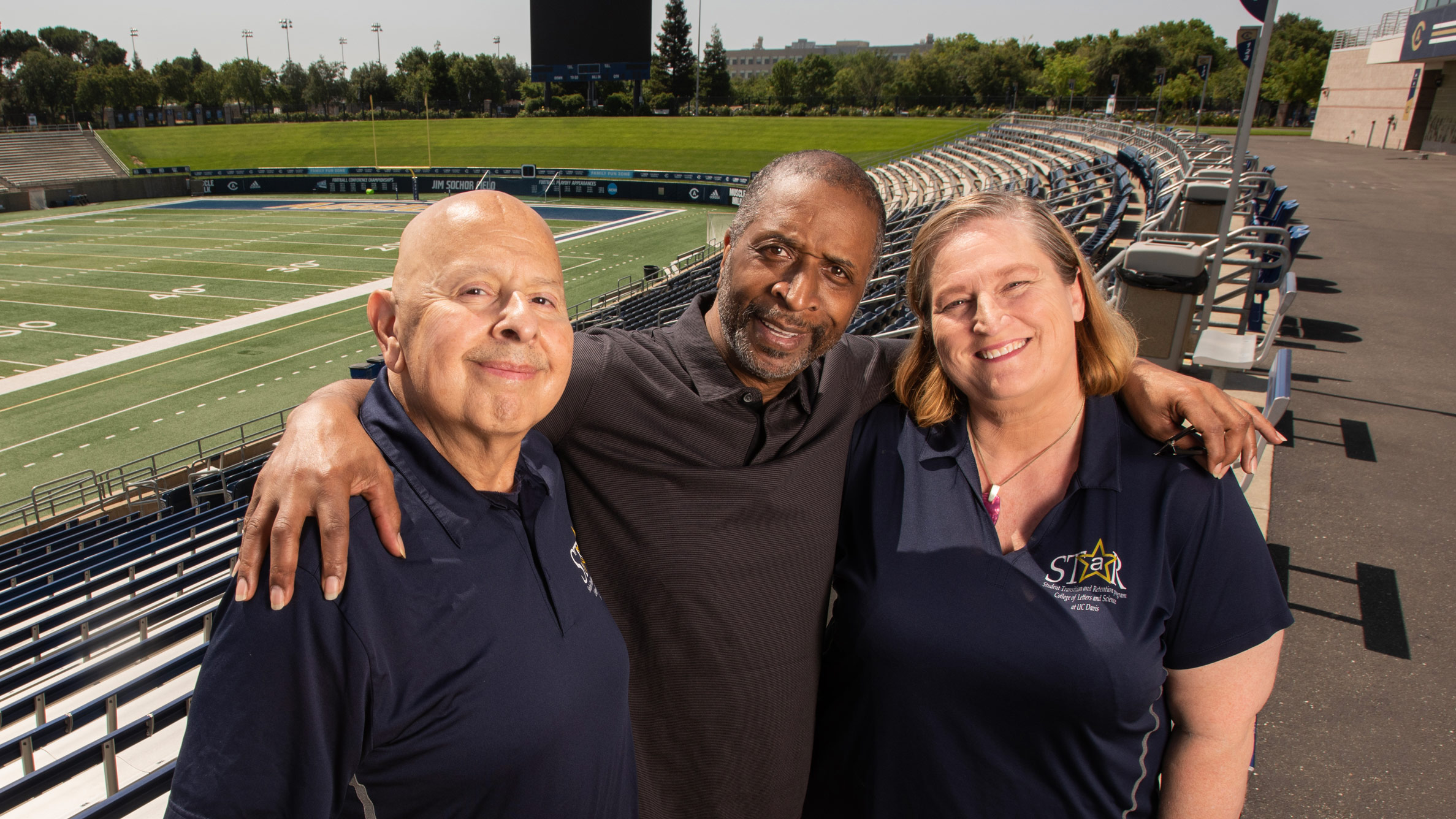 Ron Austin poses with his two advisors in the UC Davis College of Letters and Science STaR program in front of the stands with the football field visible behind them.