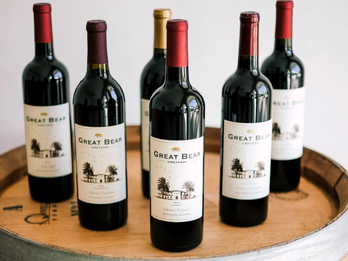 Six red-wine bottles arranged on a wooden barrel top