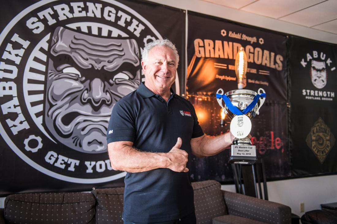 Rudy Kadlub smiles and holds up his 2018 IPL Master Cup Best Lifter trophy in his Kabuki Strength office.
