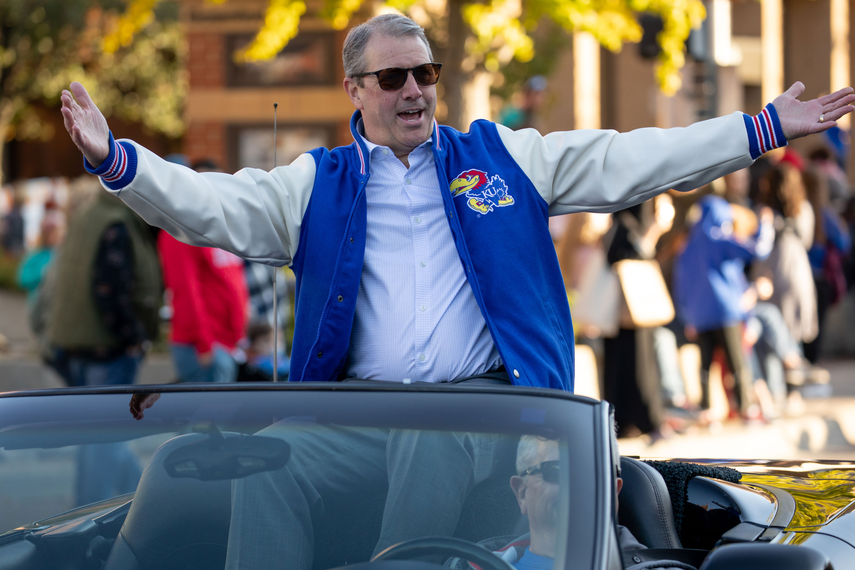Doug Girod welcomes the crowd at the homecoming parade with arms outstretched wearing a KU jersey and seated on top of a convertible.