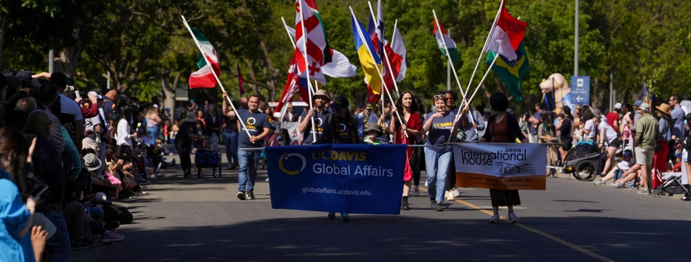 Group of Global Affairs staff and community members holding various countries' flags while marching in a parade.