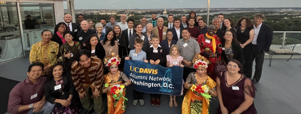 The group of attendees, association representatives, and Santi Budaya dancers wearing traditional Indonesian attire posing for a group photo on the rooftop of Top of the Town with the Potomac River and Capitol building visible in the background.