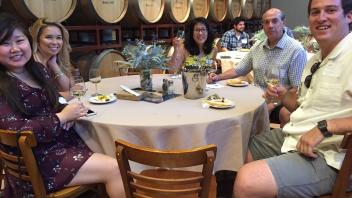 Aggies sitting at a round table near barrels of wine 