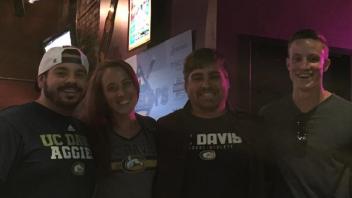 Three men and a women wearing Aggie gear, smiling.