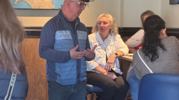 A man in a cap speaks to a group in a cozy restaurant setting.