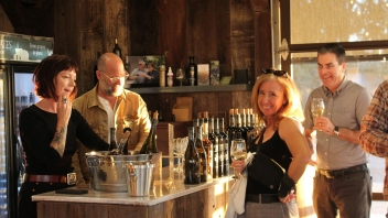 Group of four people standing next to wine glasses on a kitchen island drinking wine. 