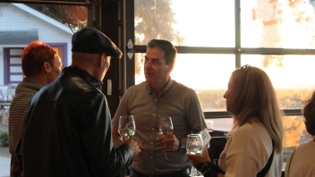 Man holding a conversation and drinking wine with two other people. 
