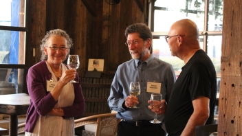 Attendees smiling and drinking wine. 