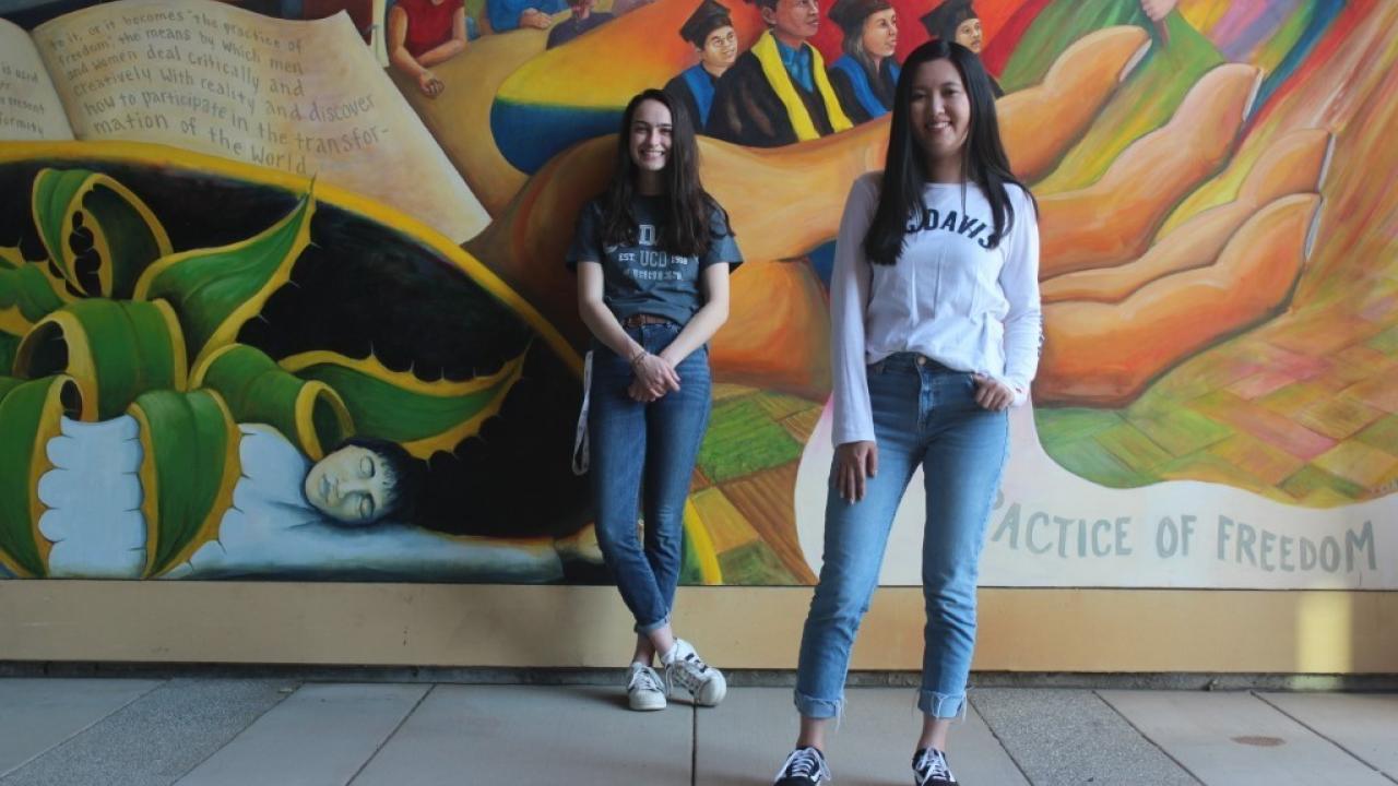 Picture of Aggie House Co-founders Ashley Lo (right) and Alan O'Brien. Both are standing in front of a colorful mural.