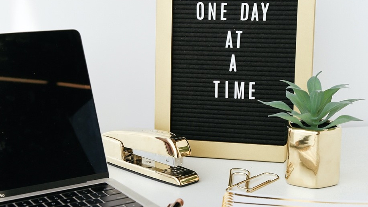 laptop work station with a sign next to it that says "one day at a time"