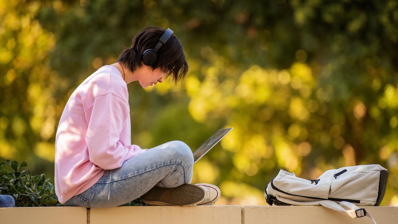 student sitting outdoors with laptop