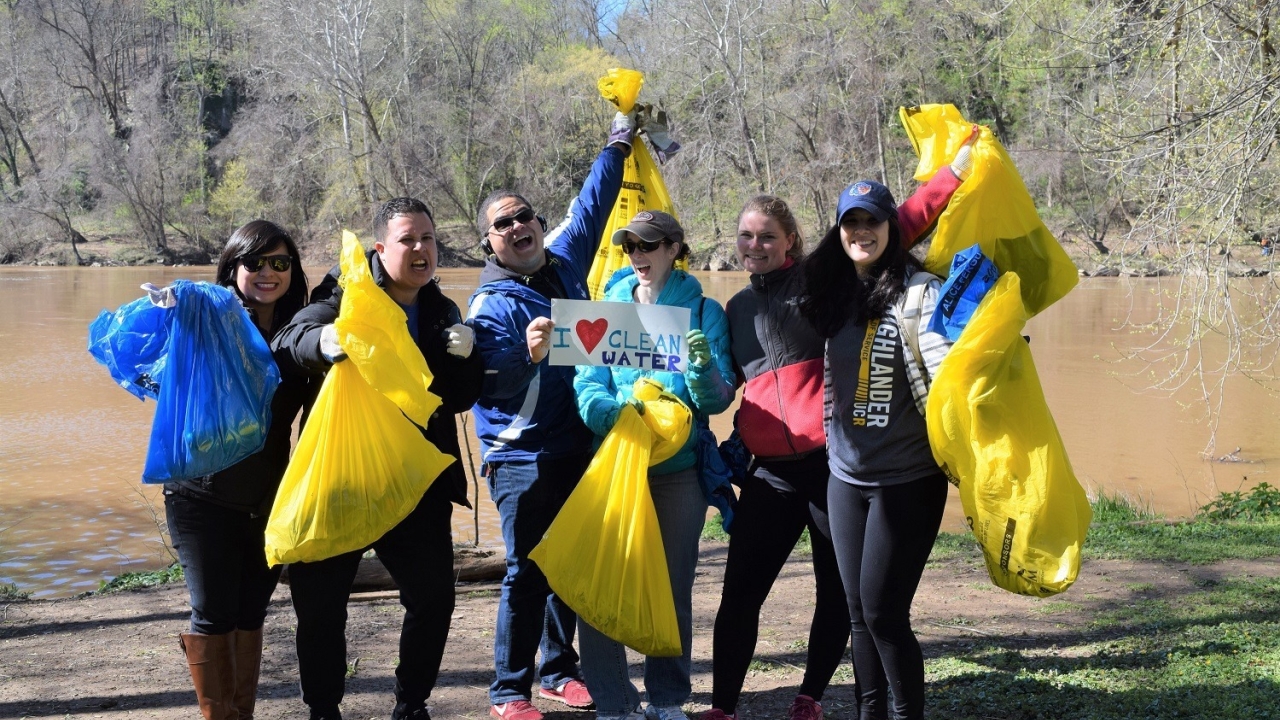 Picture of six people standing along the Potomac holding up trash bags and a sign saying "I <3 Clean Water".