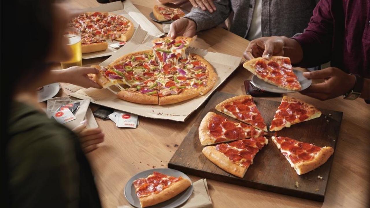 picture of three pizzas on a table with people picking up slices