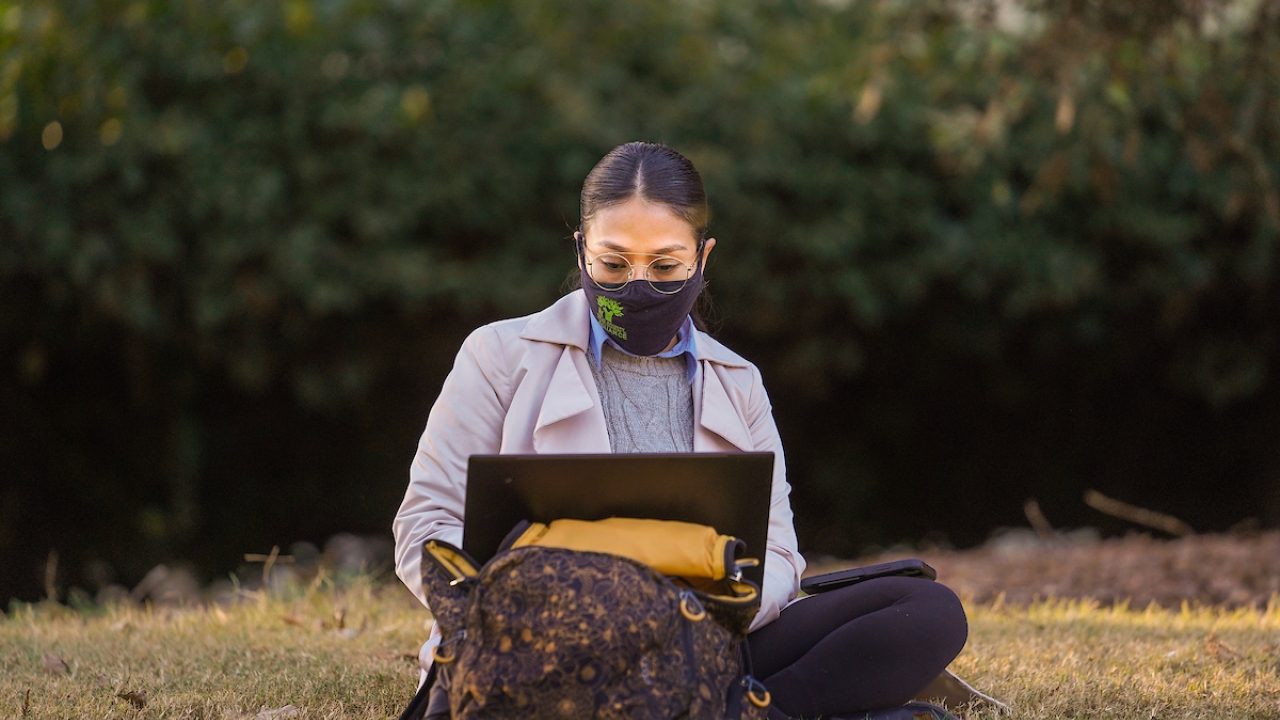 image of a student with a facemask using a laptop outside