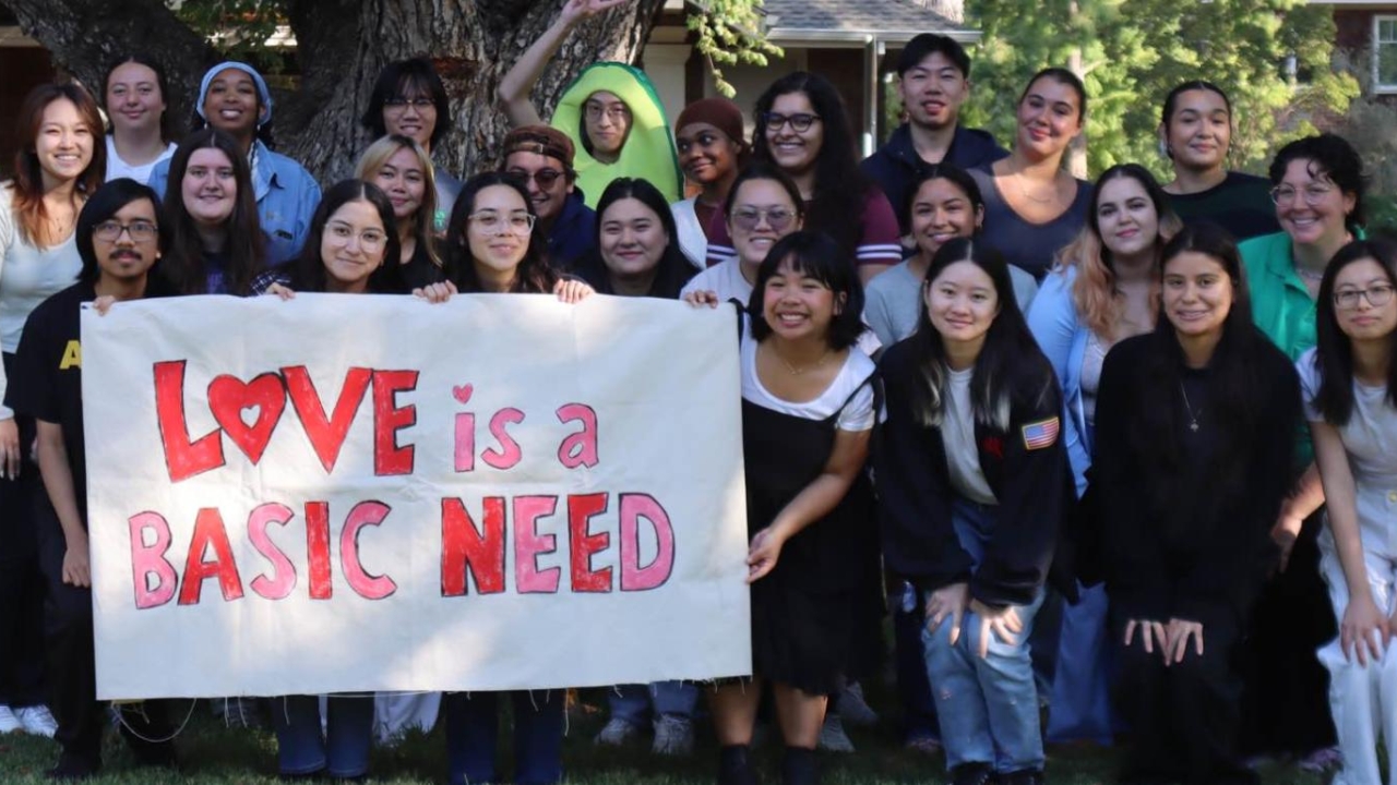 Group of Aggie Compass workers holding up a sign that says "Love is a Basic Need"