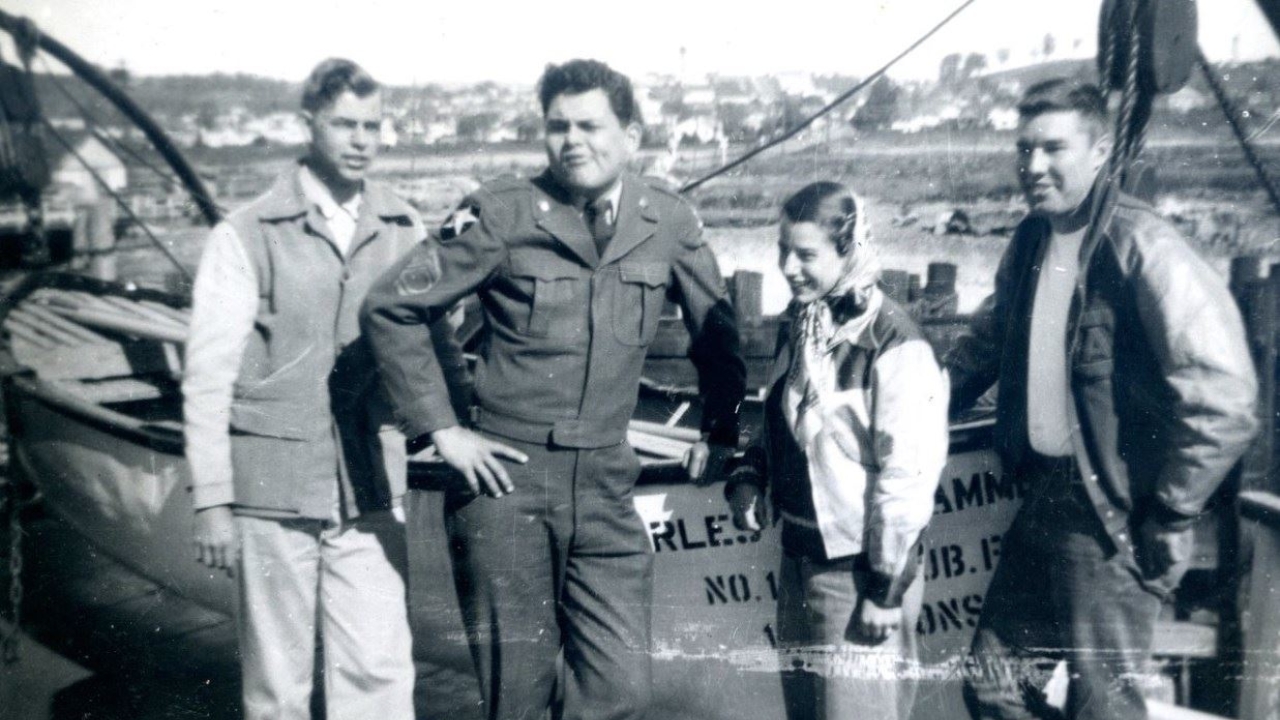 Black and white photo of four Aggie rifle team members standing next to a ferry.