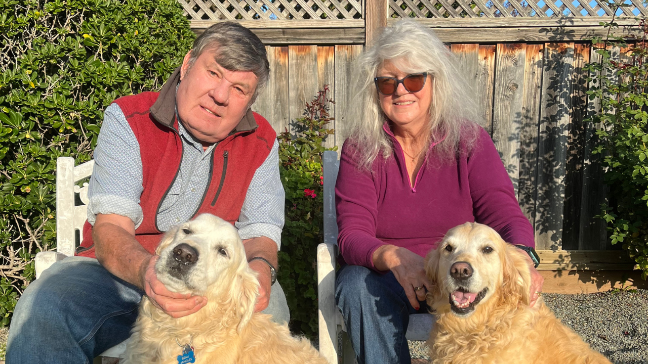 Richard Buchner and his wife, Terri seated outdoors, each with a golden retriever