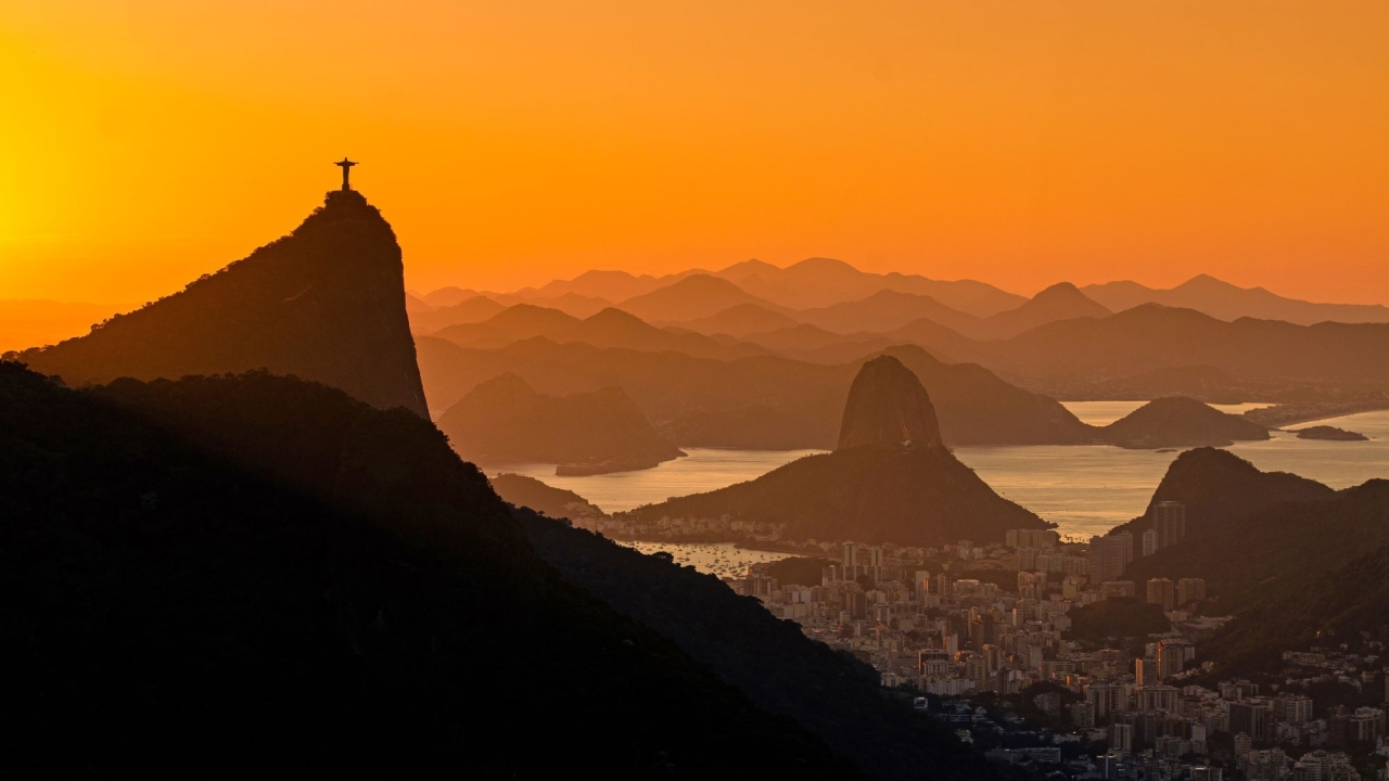 Sunset view over mountains and city, with Christ the Redeemer statue silhouetted.