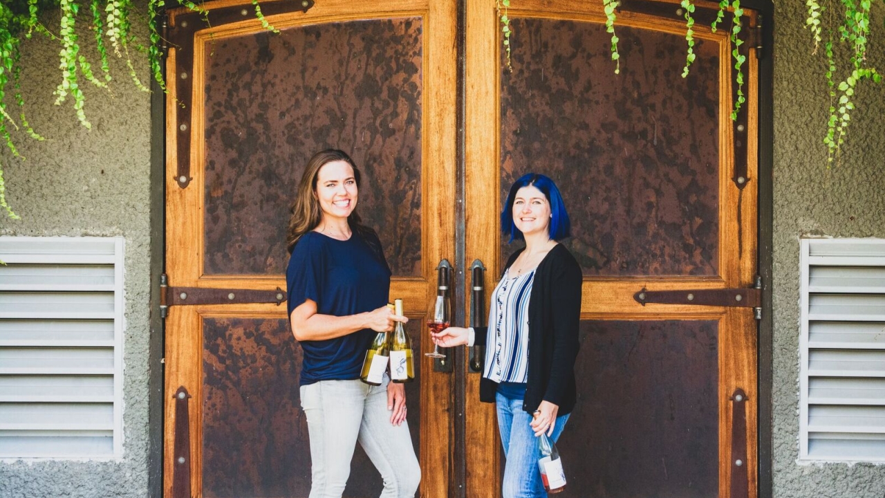 Shaina Harding and NC pose in front of door holding wine bottles