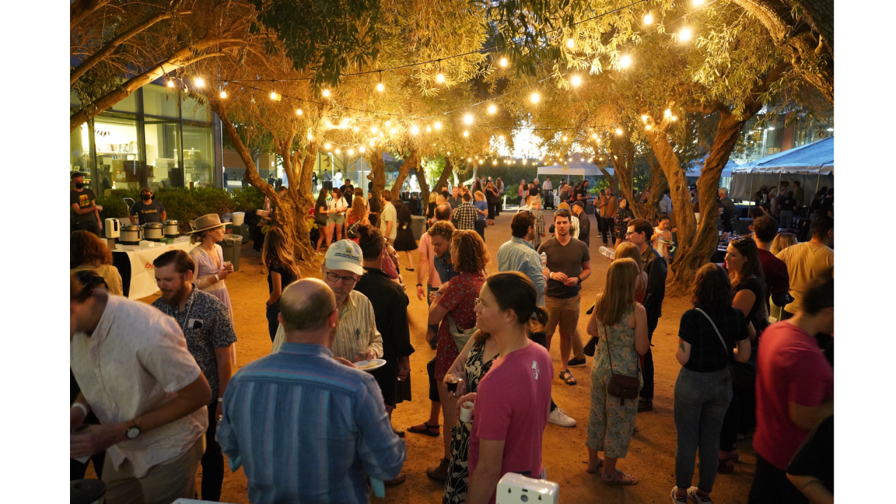 image of a group of people mingling under lights outside during the evening