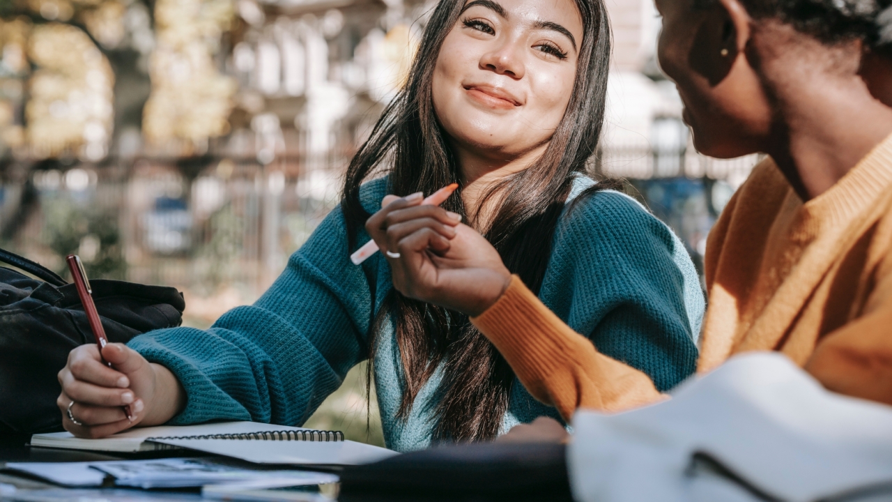 Image of two students taking notes and talking to each other