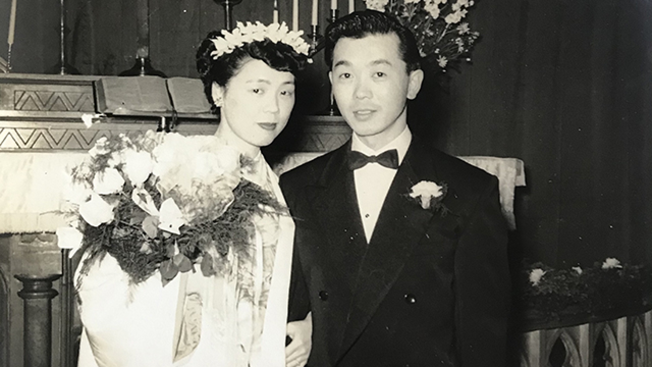 Black and white photo featuring two people in wedding attire with candles and cross behind them.