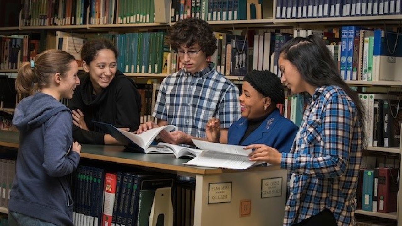students standing in a library looking at textbooks