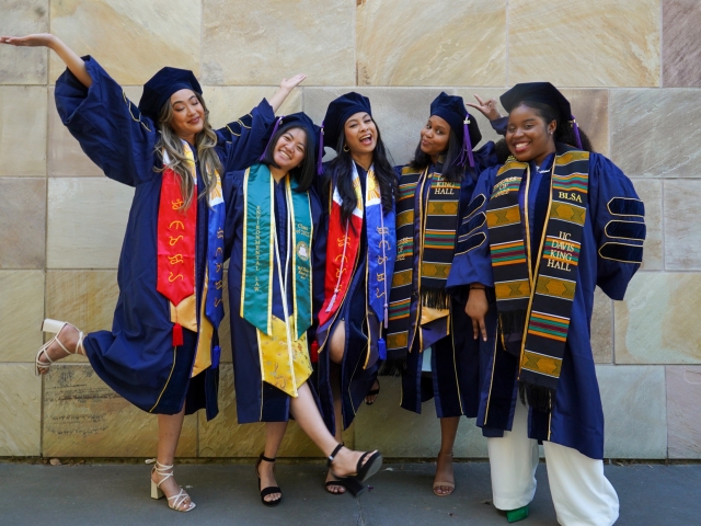 A group of UC Davis School of Law graduates pose for a photo in regalia and various stoles.