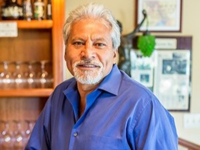 Smiling older man with gray hair and beard in blue shirt, bar interior portrait photo