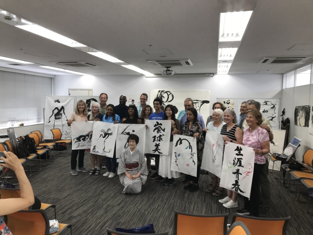 A diverse group of people holding calligraphy artworks in a classroom setting.