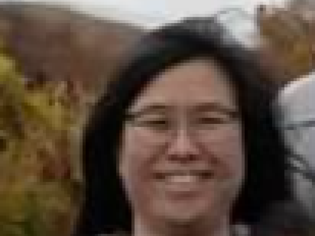 Smiling woman with short black hair and glasses, autumn background