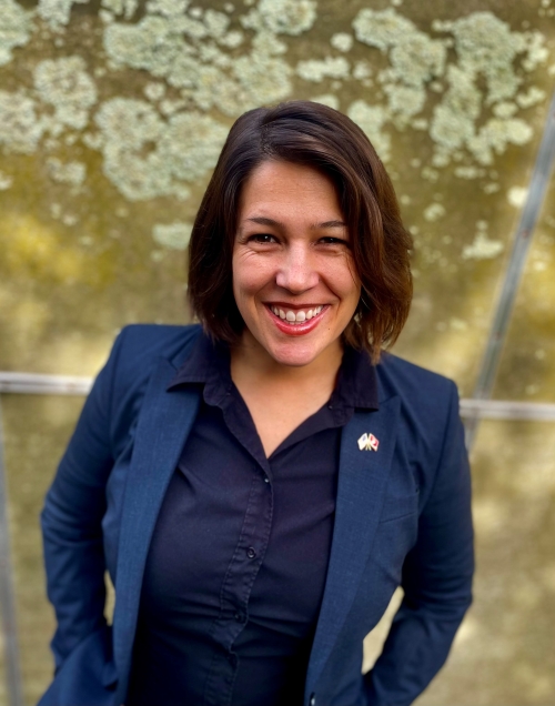 Maggie Mello smiling in business attire against a green wall.