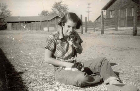 Black and white photo of Audrey West sitting at the livestock pens holding puppies in 1952.