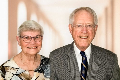 Cathy and Bob Kerr wearing business casual attire in front of a blurry background with pillars.