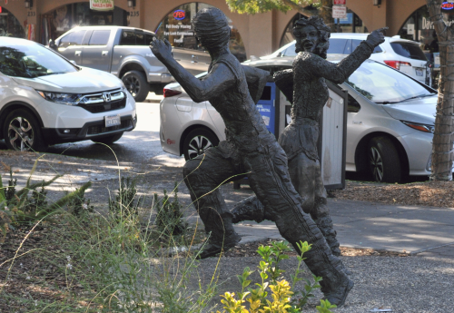 Bronze statue of two people jogging in opposite directions and looking at each other. One points the way for the other to follow. 
