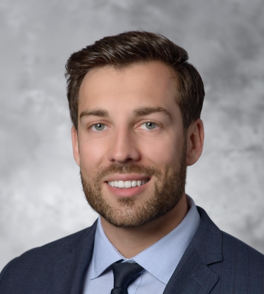 Headshot of Artem Trotsyuk posing in front of a grey backdrop wearing a dark blue blazer and tie with a button-down shirt.