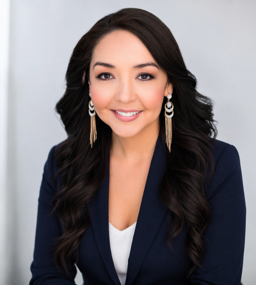 Smiling professional woman with long dark hair, navy blazer and dangling earrings (headshot photo)