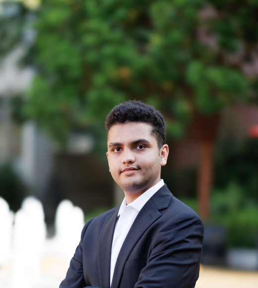 Headshot of Shayvia Padia posing outdoors in front of a tree wearing a dark blazer and button-down shirt.