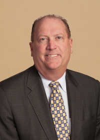 Middle-aged male poses for a headshot wearing a grey suit, white and light blue checkered button-down shirt, and gold and blue tie.