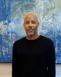 DeWayne Quinn poses in a black long-sleeved shirt in front of a large framed painting indoors.
