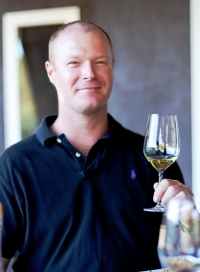 Kirk Venge wearing a black shirt holds up a glass of red wine.