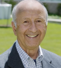 Roy Shlemon poses in a dark blazer and gingham button-down shirt in front of a lawn.