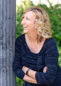 Blonde, curly haired woman smiling and looking up to the left with her arms crossed