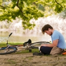 a student studies under a blooming tree in the arboretum next to their bike