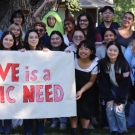 Group of Aggie Compass workers holding up a sign that says "Love is a Basic Need"