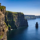 Cliffs rise sharply from the calm blue ocean under a clear sky.